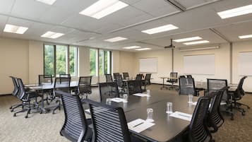 Une salle de conférence dotée d’une grande table, de chaises noires, d’un tableau blanc et de grandes fenêtres.