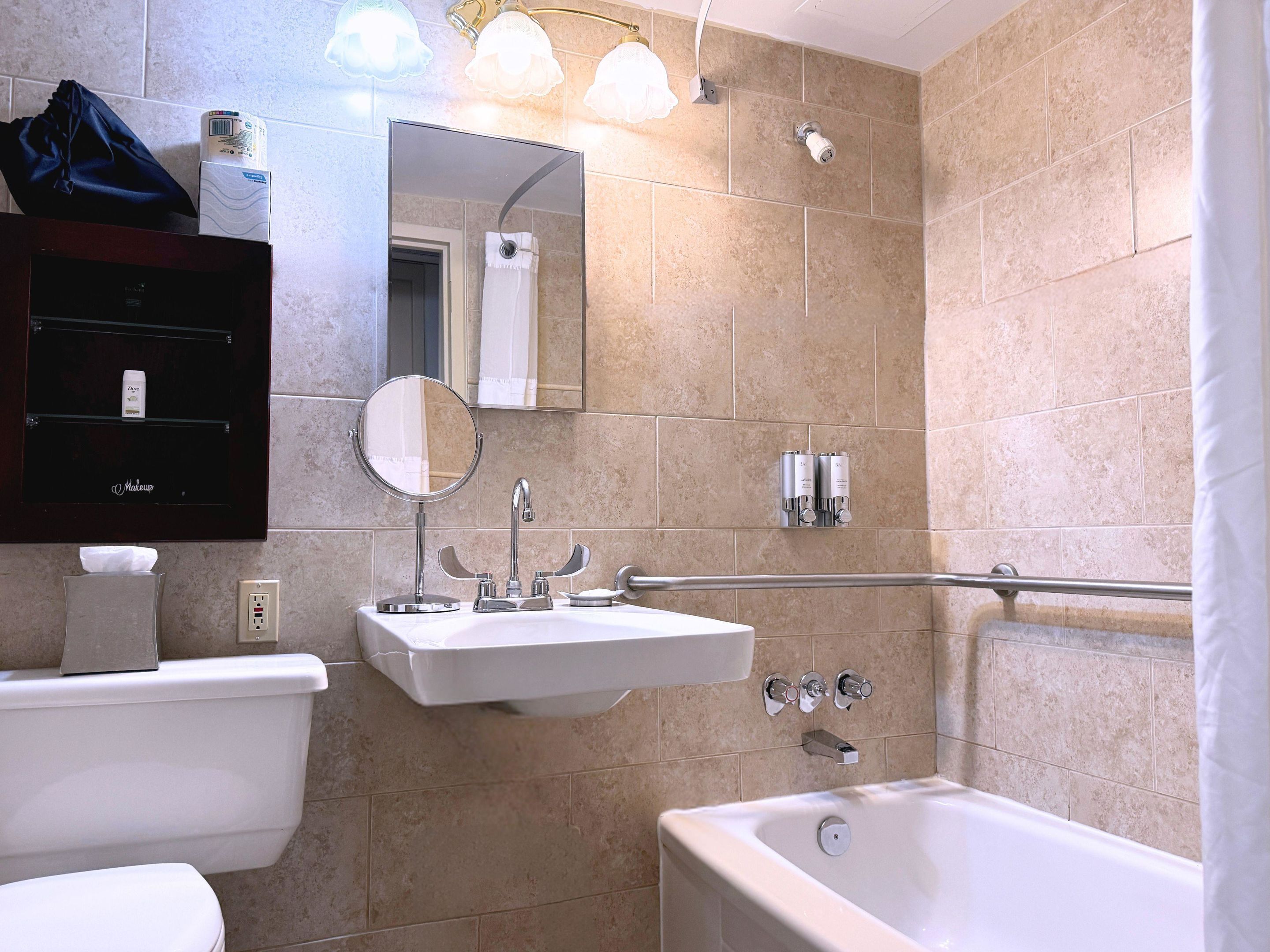 Un baño con inodoro, lavamanos, espejo, ducha y perchero para toallas.