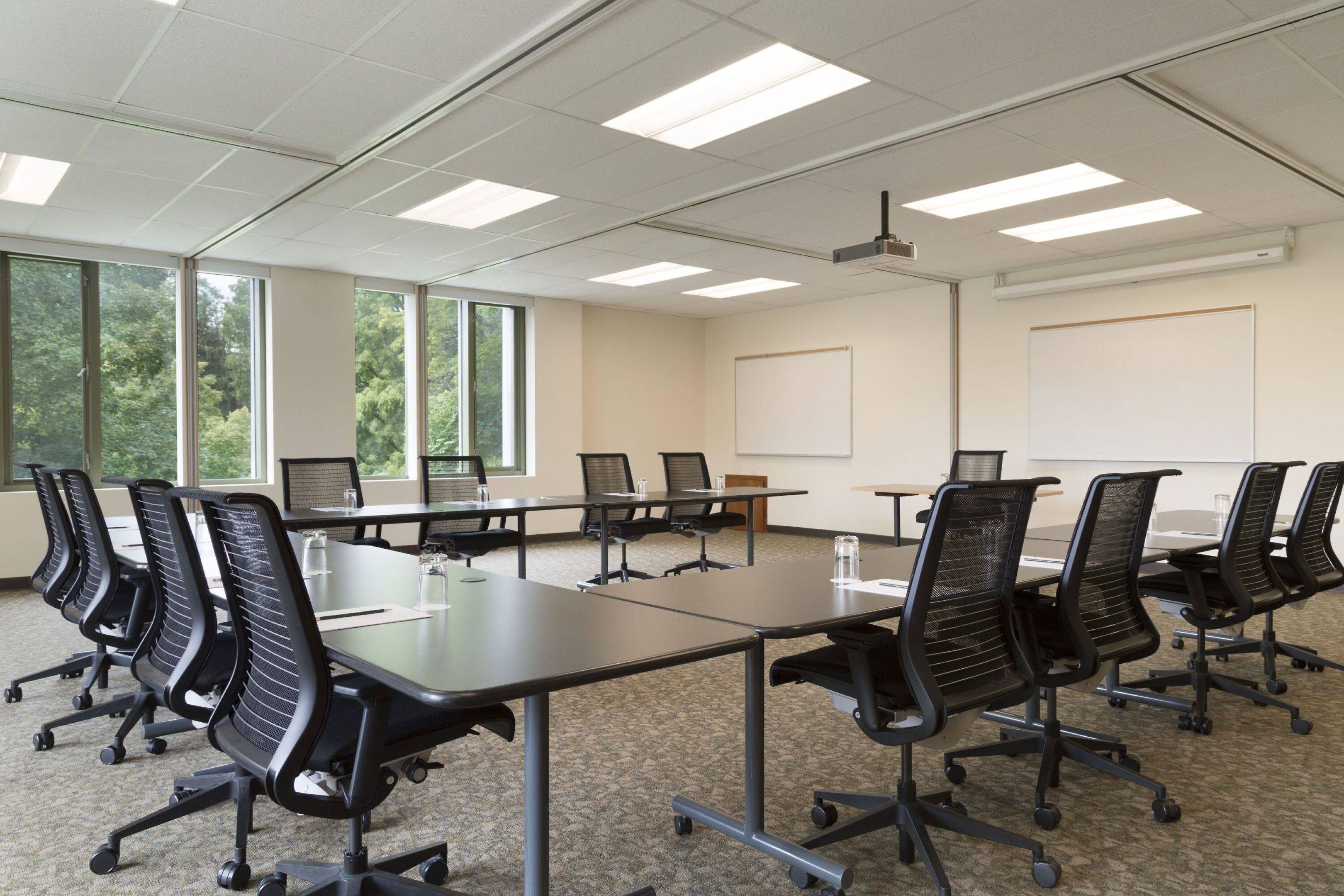 A conference room with a long table, black chairs, carpeted floor, large windows, and a projector.
