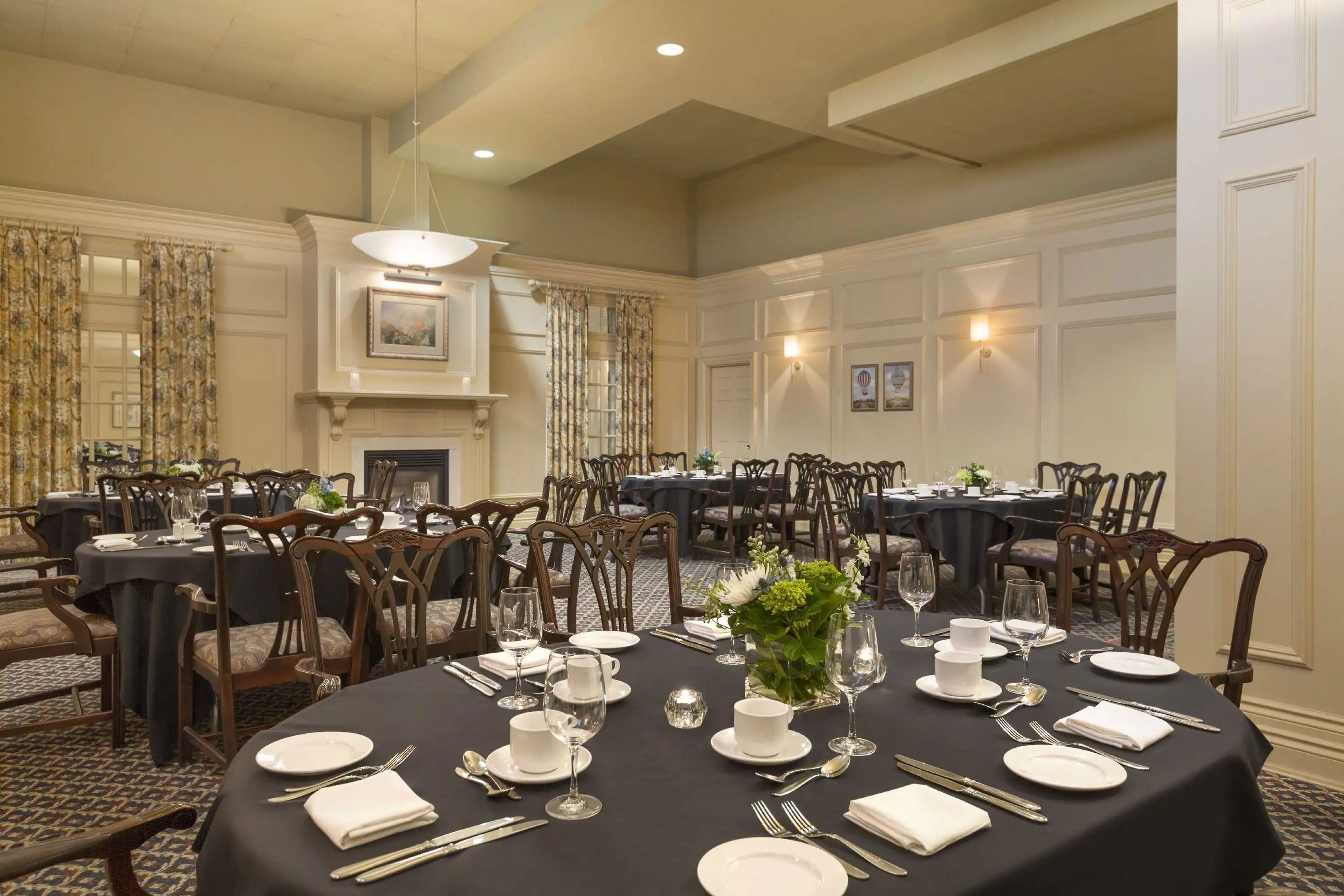 A formal dining room with multiple tables set for service, a fireplace, and framed artwork on the walls.