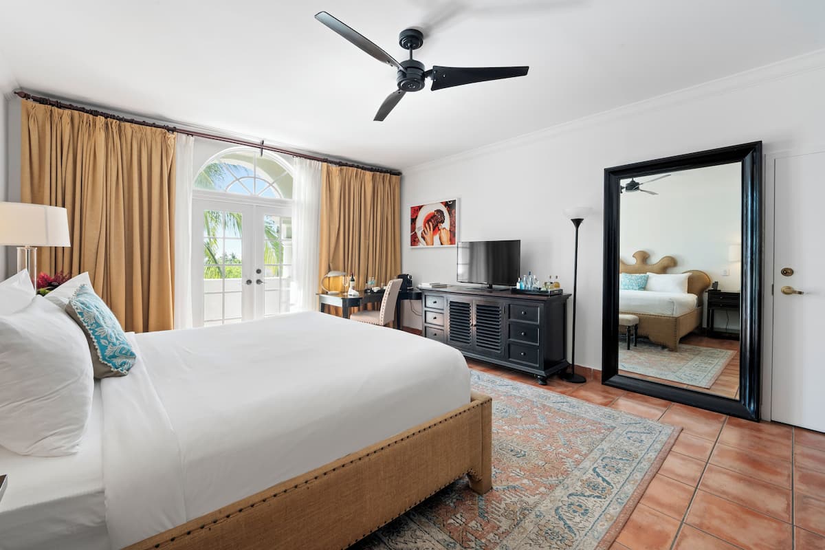 A spacious bedroom with a large bed, a ceiling fan, a television, and a wardrobe.