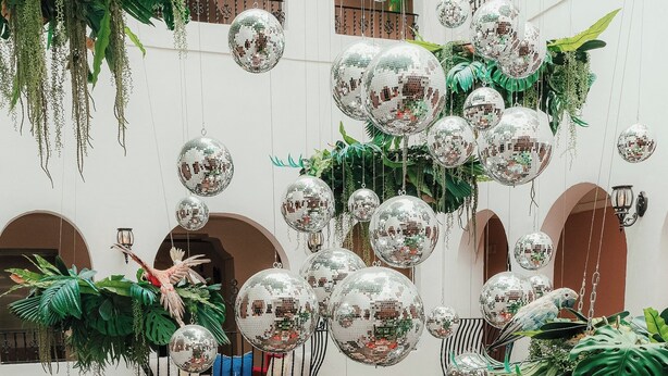 Ett rymligt inomhusområde med högt i tak, med en sittgrupp bestående av soffor och ett soffbord, omgivet av krukväxter och hängande discobollar.
