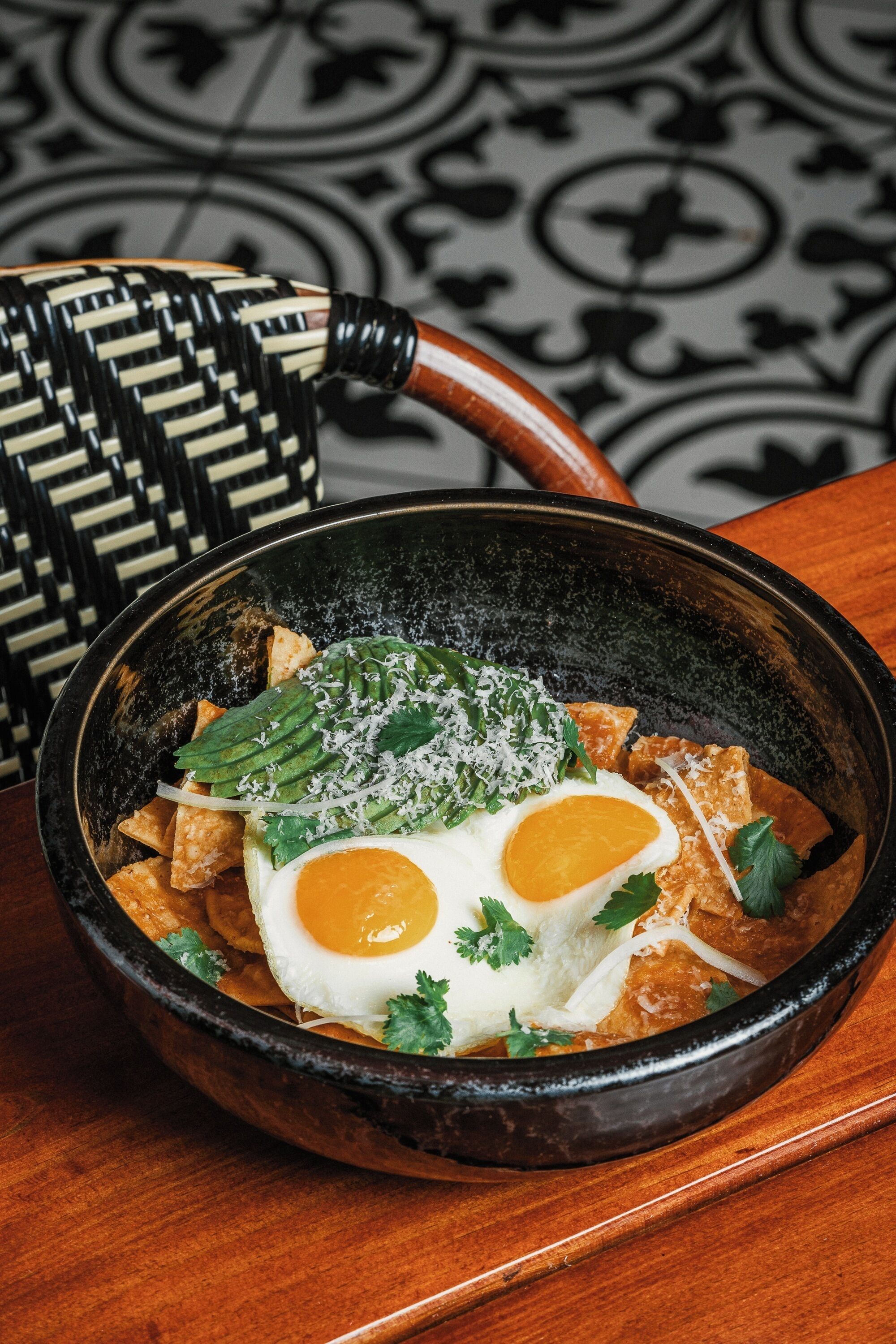 A bowl of food with eggs, avocado, and cheese on a table.