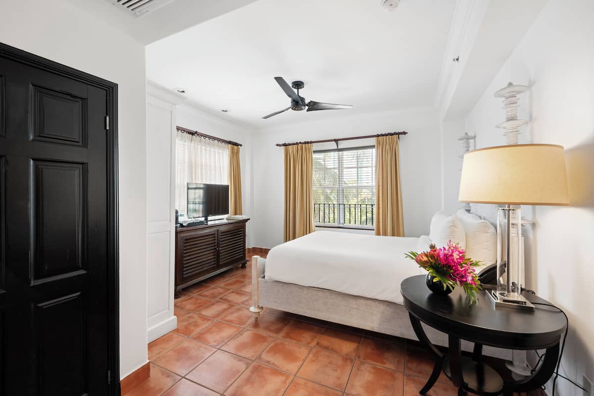 A hotel room with a bed, a desk with a lamp, a TV, and a window with curtains.