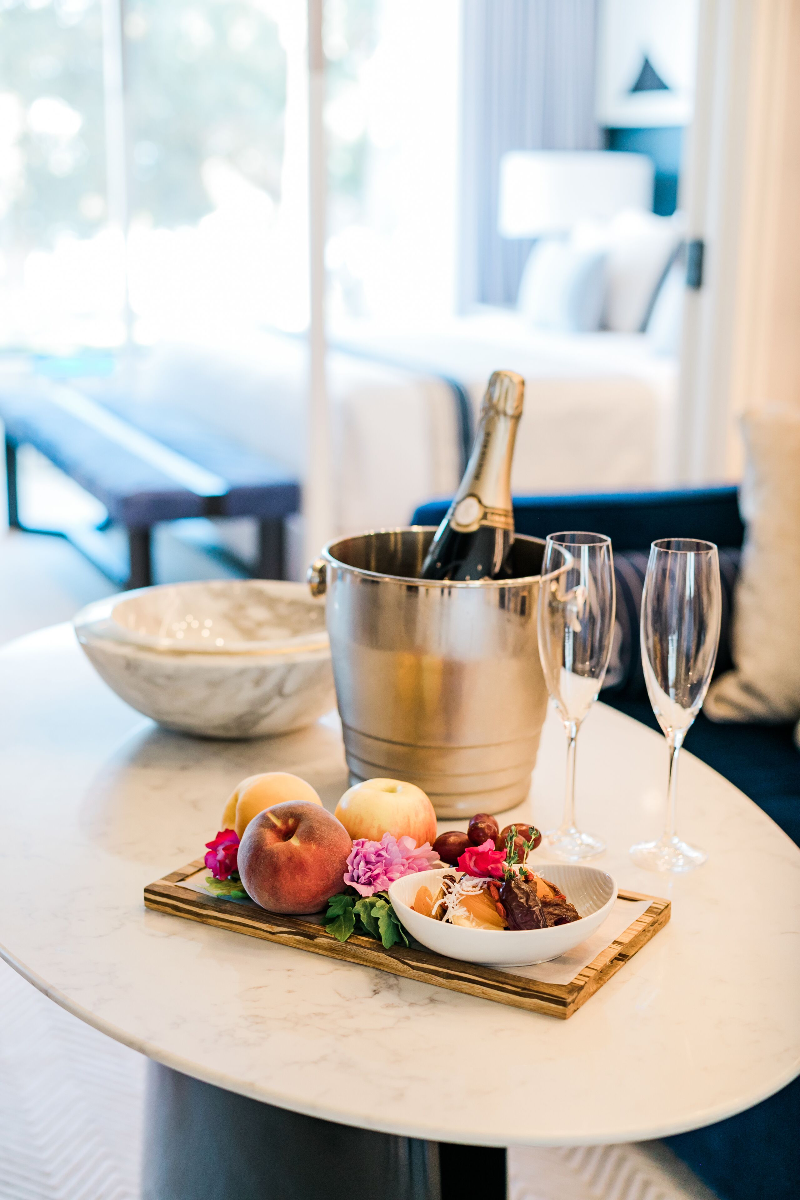 A table with a champagne bottle, two glasses, a bowl of fruit, and a plate of food.