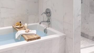 Une salle de bain moderne avec une baignoire en marbre, un plateau en bois contenant des articles de toilette et un verre d’eau.