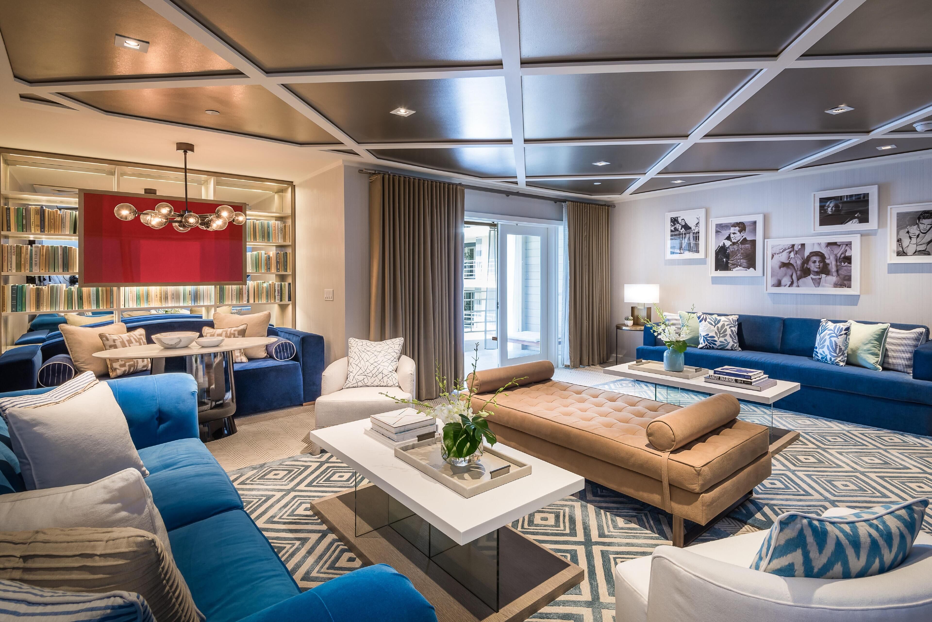 Un soggiorno moderno con un divano blu, una poltrona beige e un tavolino da caffè. Si nota una libreria con una parete di accento rossa e un soffitto con illuminazione a incasso.