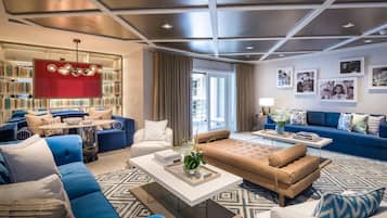 Un soggiorno moderno con un divano blu, una poltrona beige e un tavolino da caffè. Si nota una libreria con una parete di accento rossa e un soffitto con illuminazione a incasso.