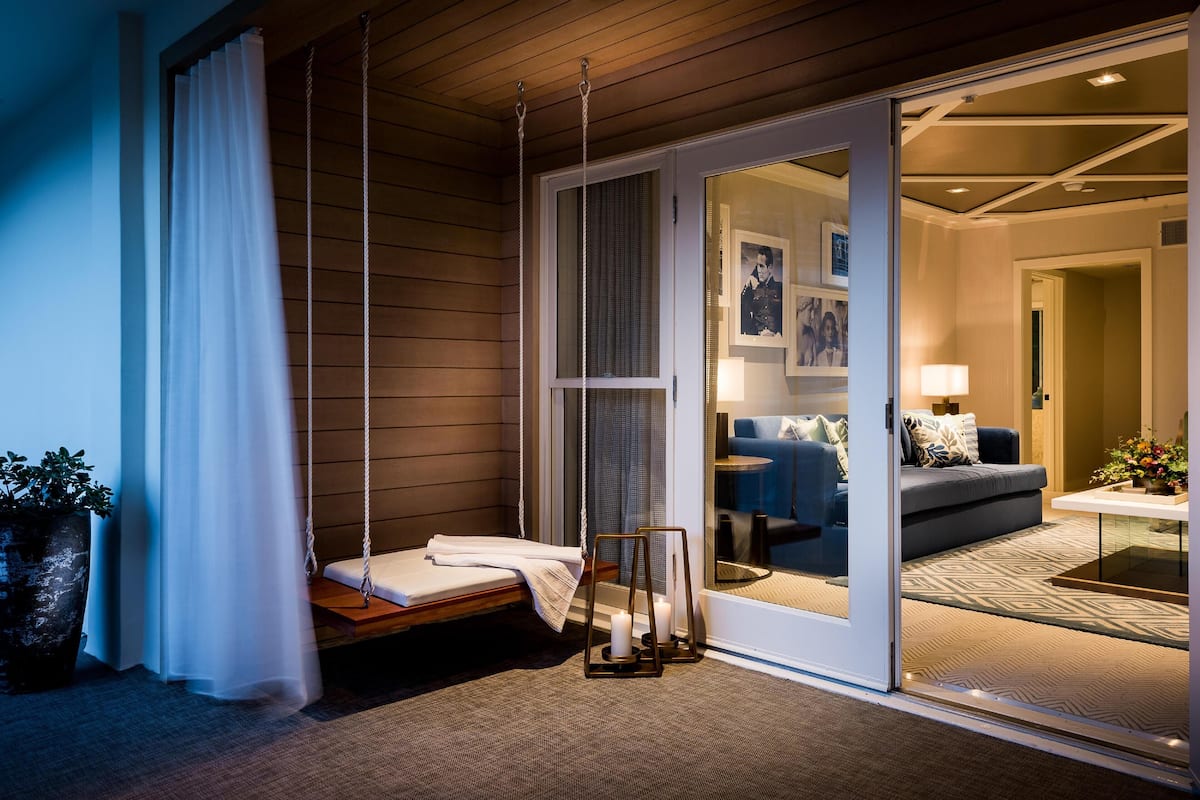 Un dormitorio acogedor con una cama, un columpio y un ventanal de vidrio que da a una sala de estar con un sofá y una lámpara.