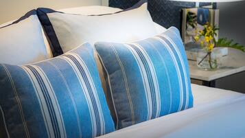 A bed with blue and white striped pillows, a white pillow, and a lamp with a plant on a bedside table.