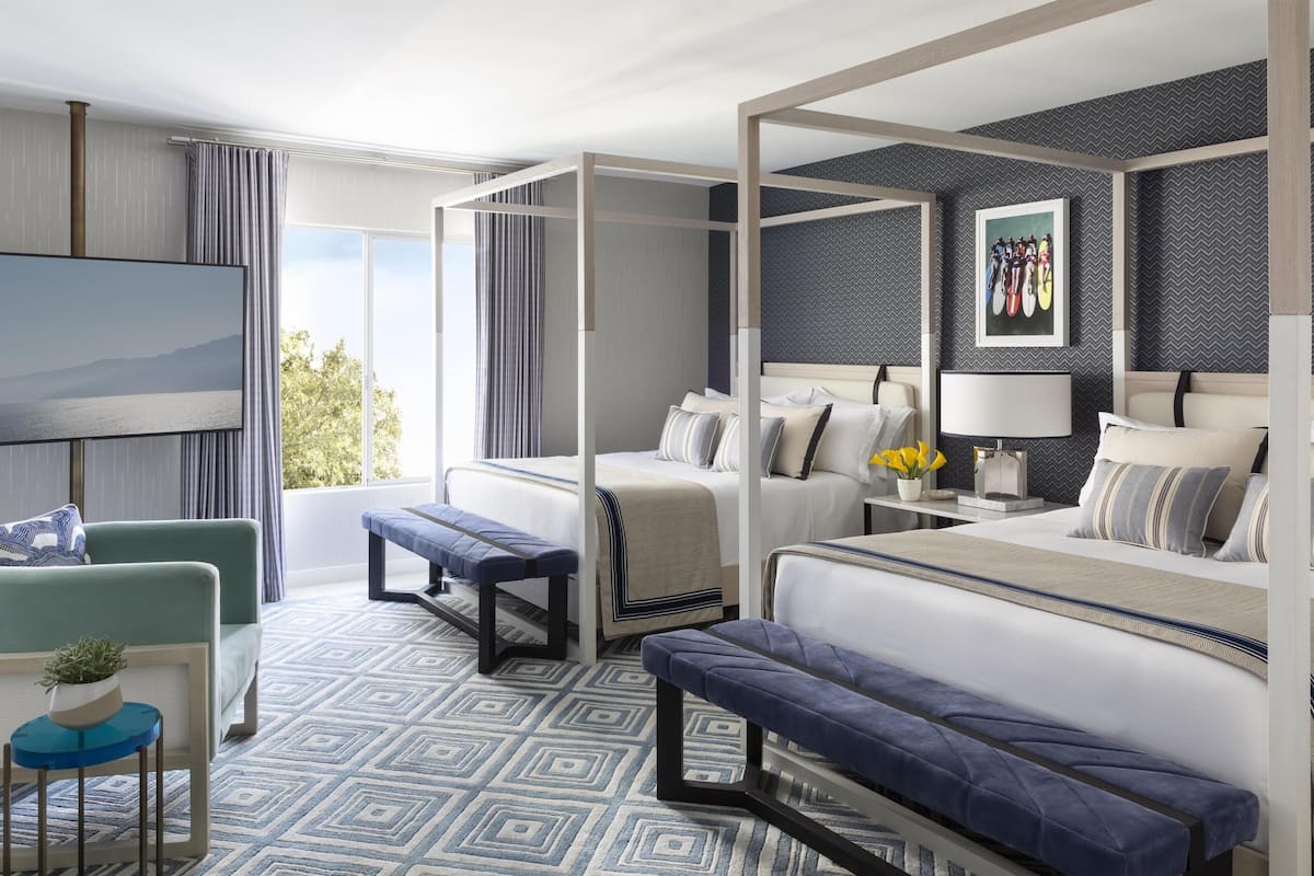 Una habitación de hotel moderna con una cama grande, una zona de estar con un banco, un televisor y vistas al exterior.