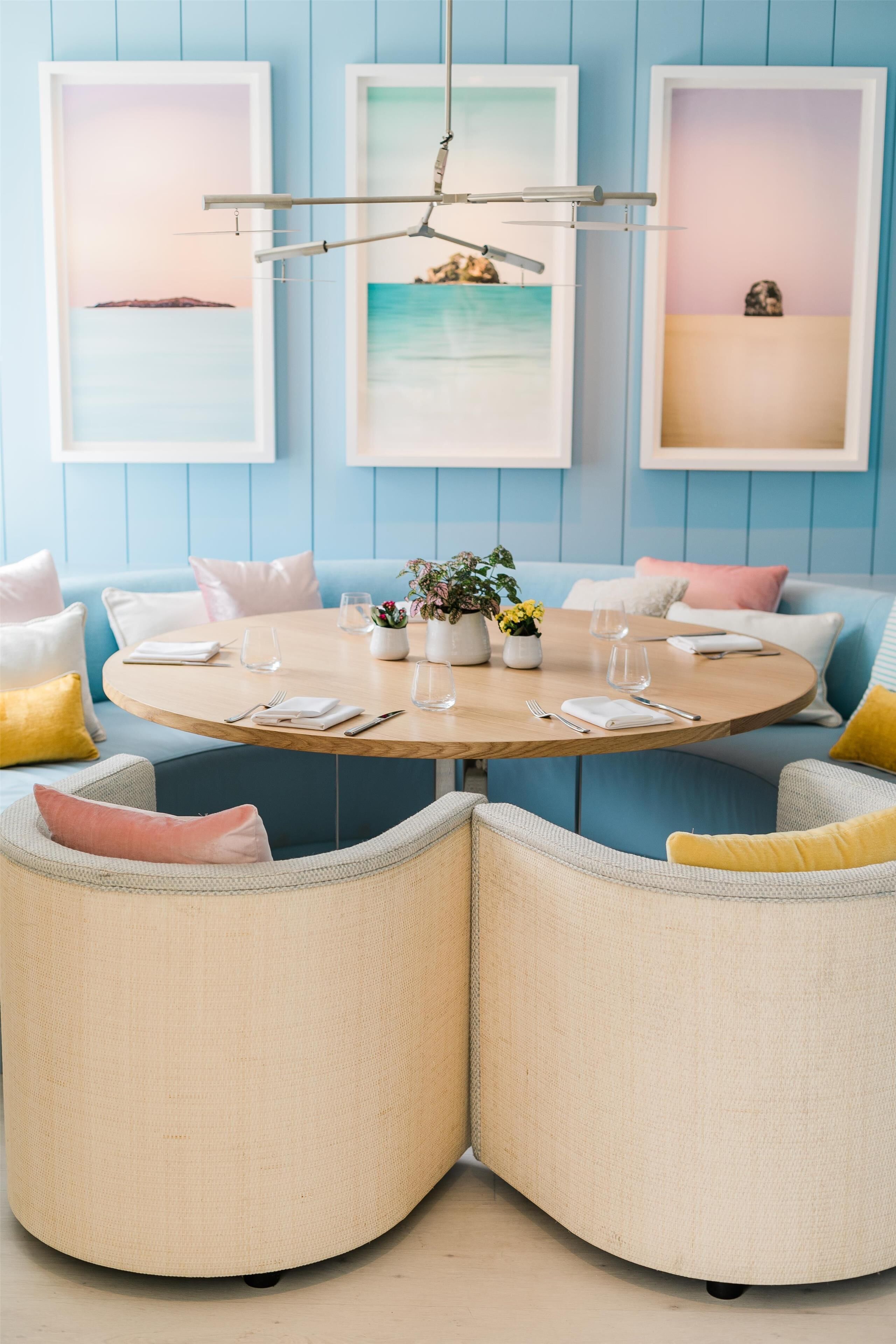 A dining area with a round table, chairs, and framed artwork on the wall.