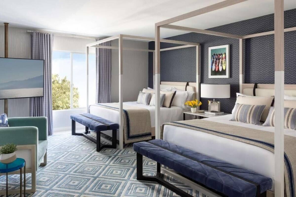 Una habitación de hotel moderna con una cama grande, televisor, sofá y balcón con vistas.