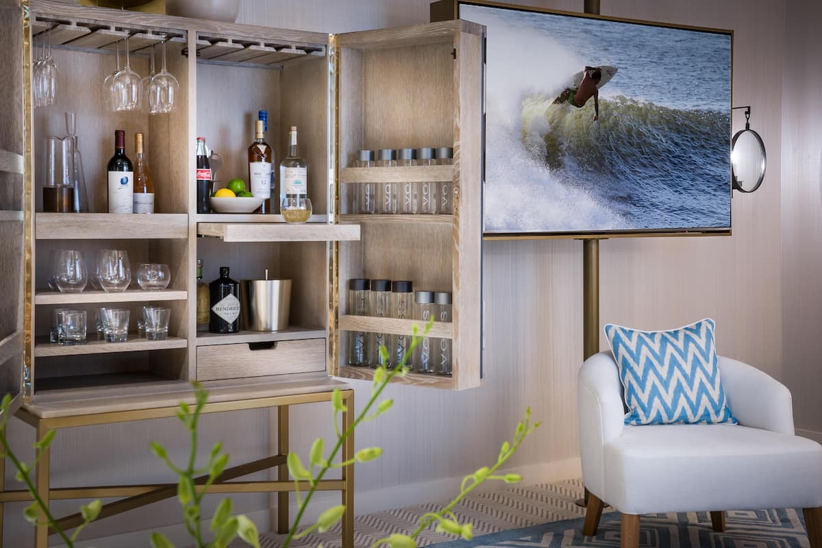 Una sala de estar moderna con un mueble de entretenimiento de madera, un televisor montado mostrando a un surfista y un sillón blanco con un cojín azul y blanco.