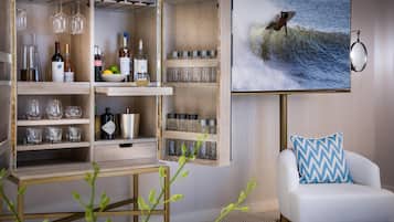 A modern living room with a wooden entertainment center, a mounted TV displaying a surfer, and a white armchair with a blue and white pillow.
