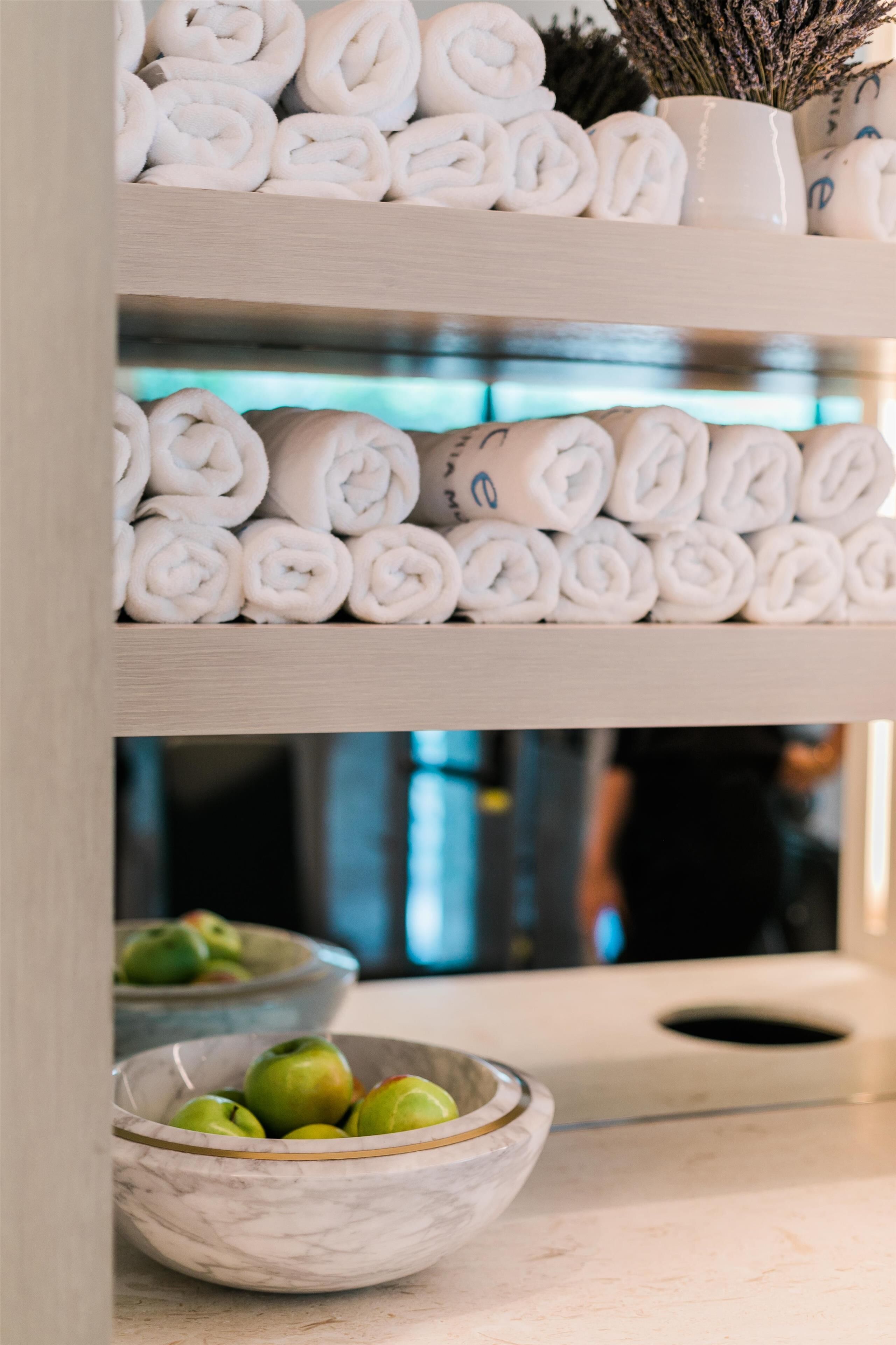 A shelf with neatly rolled towels and a bowl of green apples.