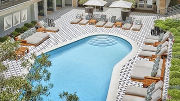 A pool area with lounge chairs and umbrellas, surrounded by patterned flooring and greenery.