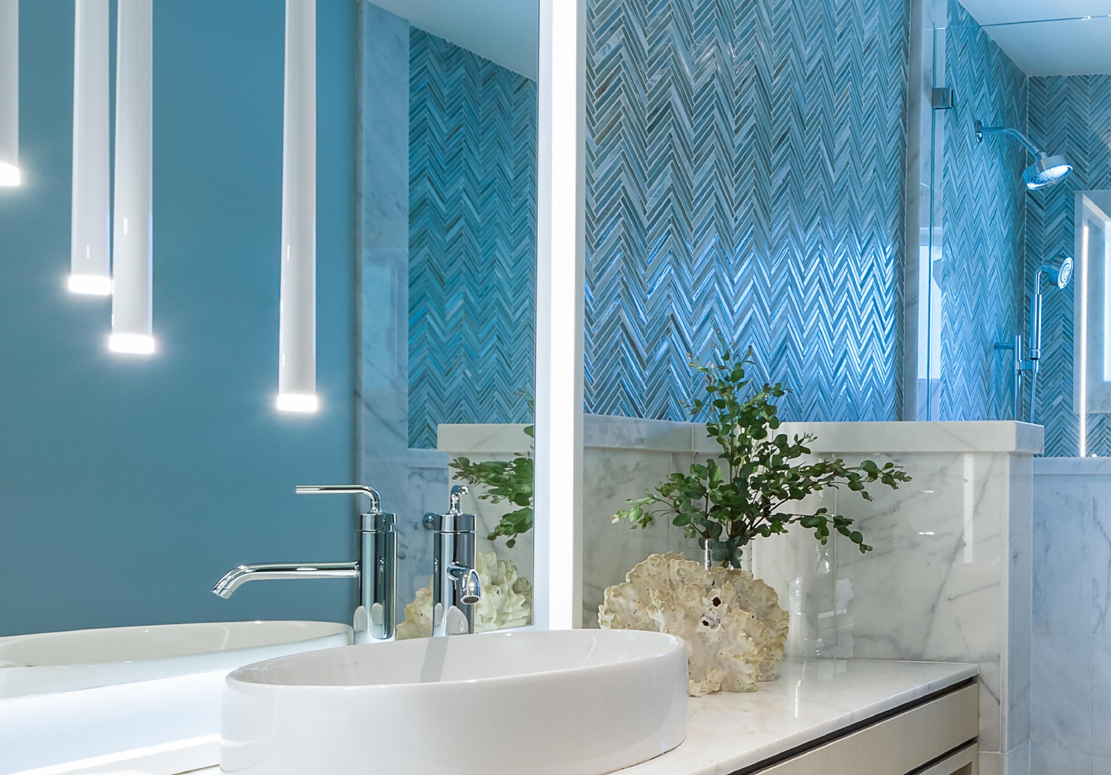 A modern bathroom with a large mirror, a white sink, and a herringbone-patterned wall.