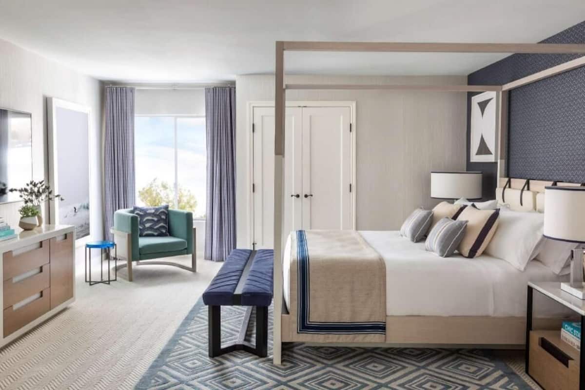 Una habitación de hotel moderna con una cama grande, un escritorio, una silla, un banco y vistas al exterior.