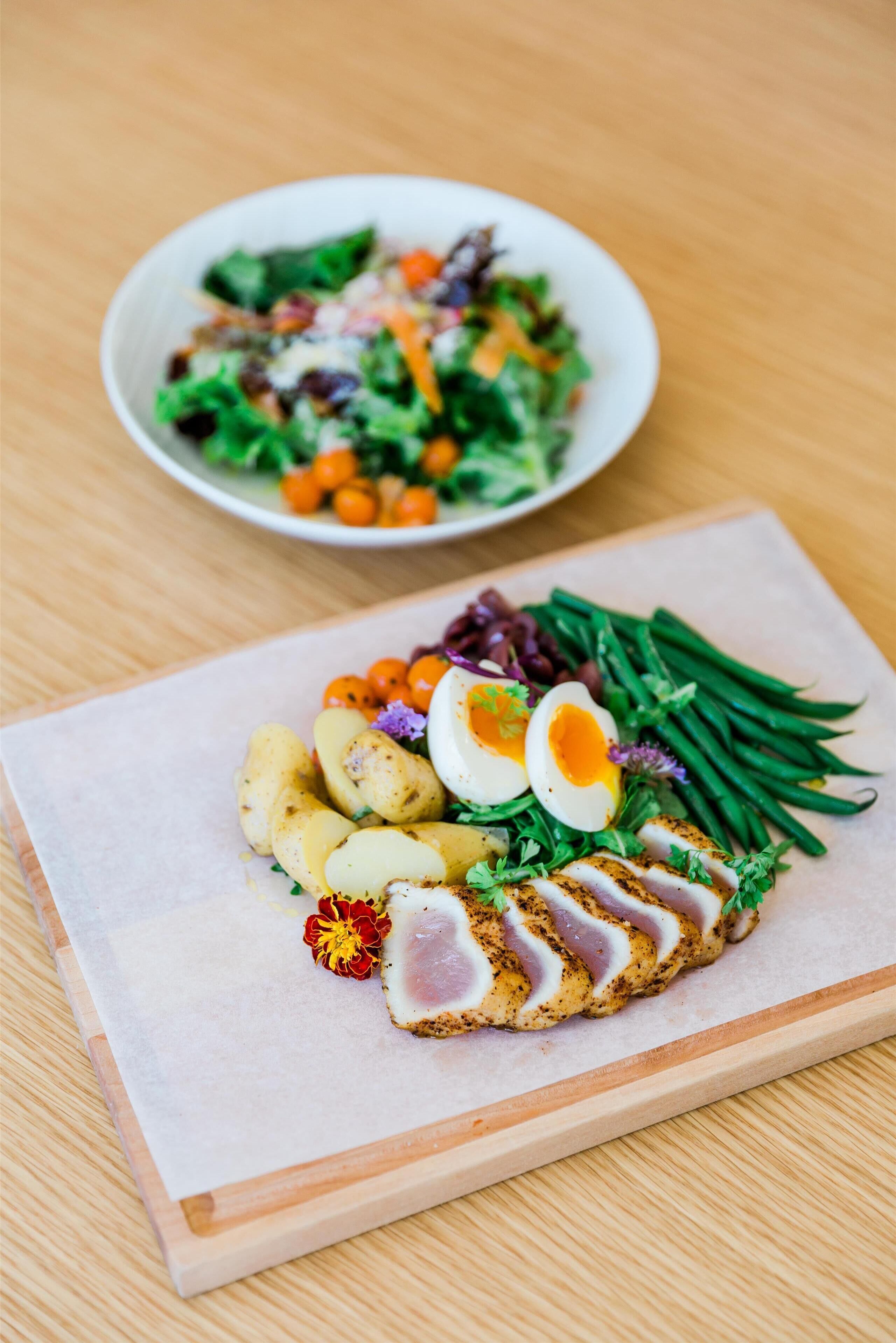 A wooden table with a plate of food, including sliced meat, boiled eggs, and vegetables.