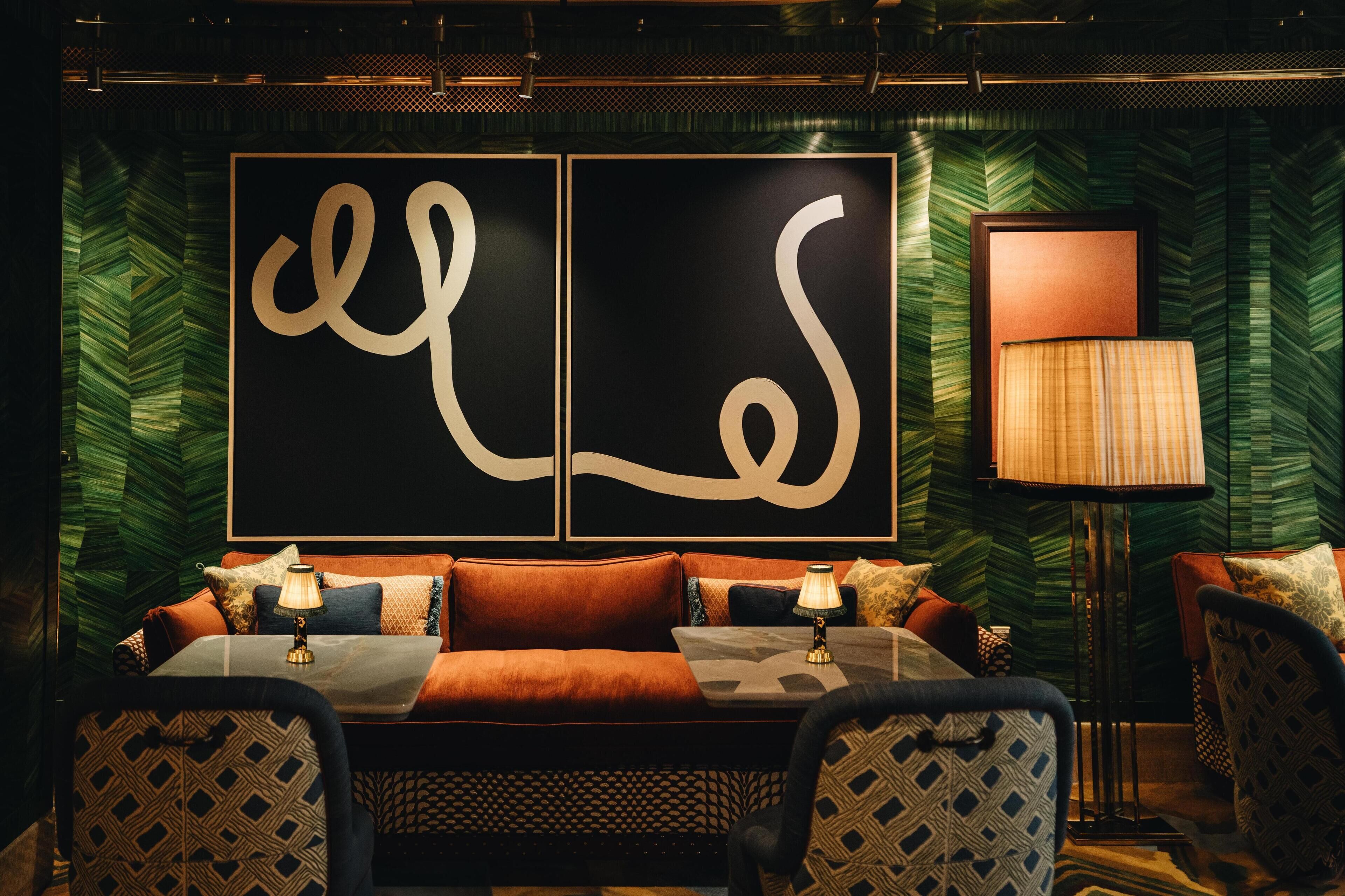 A cozy seating area with a sofa, two armchairs, and a small table, all set against a green patterned wall with large calligraphy art.