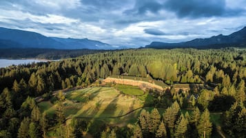 Un hotel rodeado de un bosque denso, con un campo de golf y montañas al fondo.