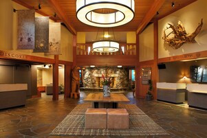 A lobby with a stone fireplace, wooden reception desk, and a large chandelier.