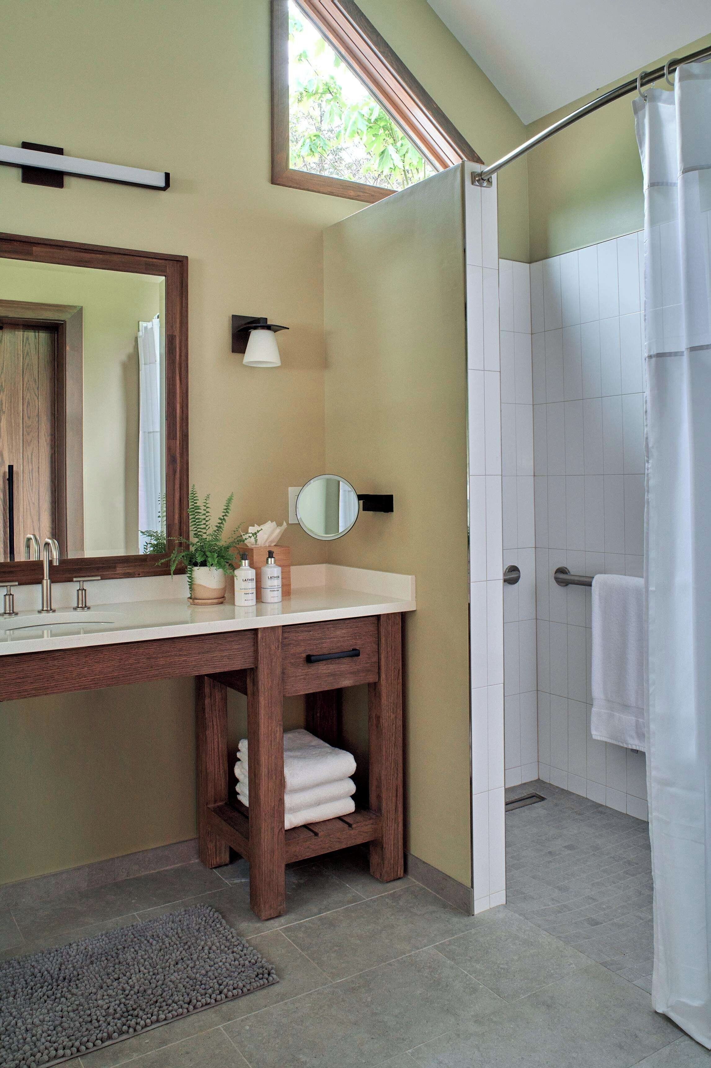 A bathroom with a wooden vanity, a mirror, a towel rack, and a shower area.