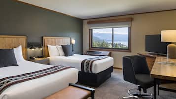 A hotel room with two beds, a desk, a chair, a TV, and a window with a mountain view.