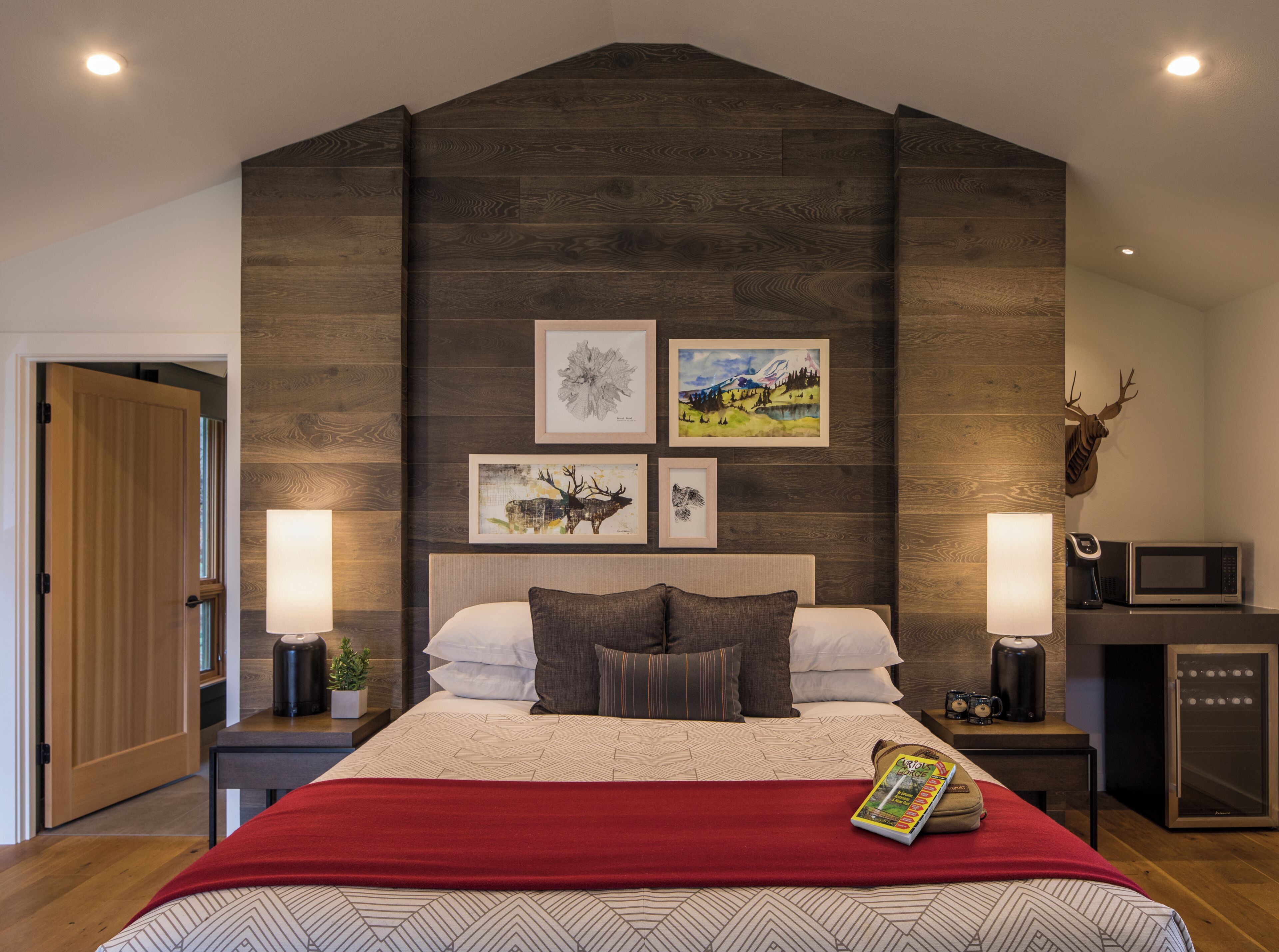 A bedroom with a bed, two bedside tables, a mounted deer head, and framed artwork on the wall.