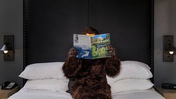 Una persona disfrazada con un pelaje sentada en una cama con un libro titulado 'Ever Wild' de Darryl Lloyd, leyendo en una habitación con un cabecero oscuro y lámparas de noche.