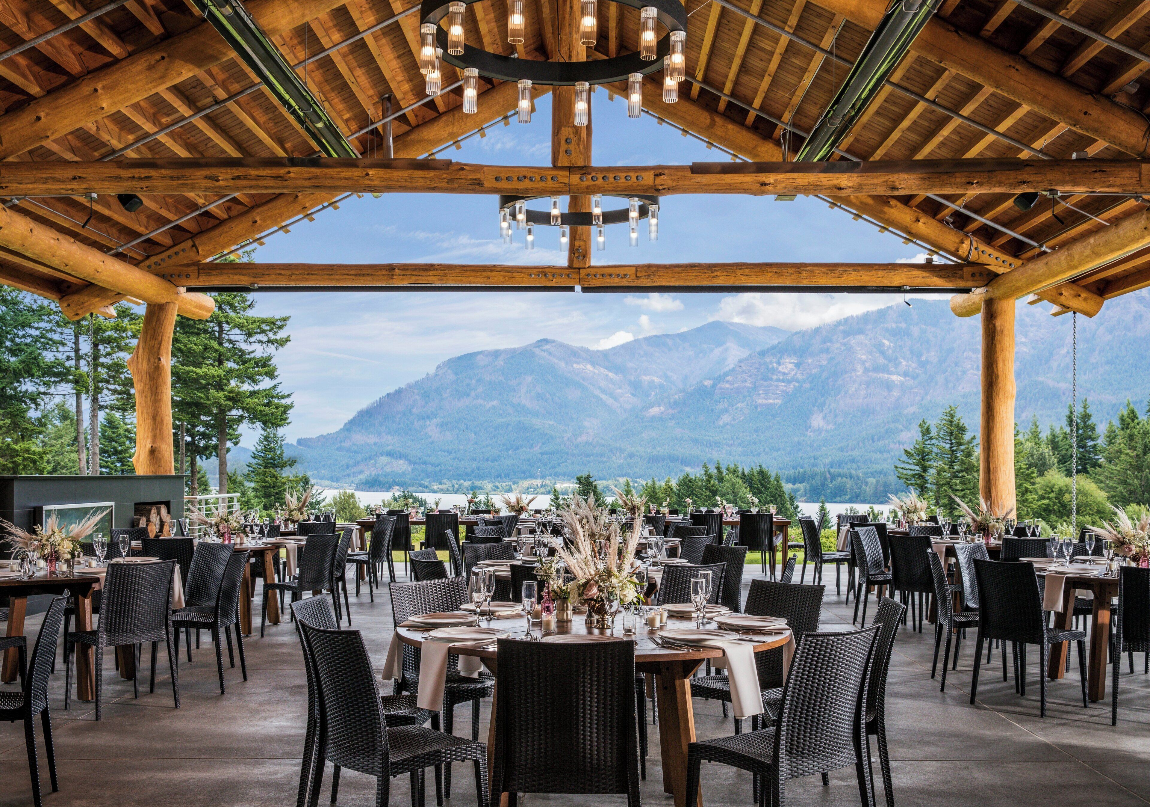 An outdoor dining area with tables and chairs, a wooden ceiling, and a mountain view.