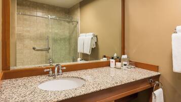 A bathroom with a granite countertop sink, a large mirror, and a shower area.