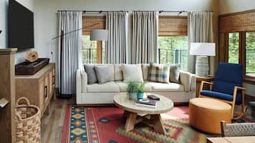 Una sala de estar con sofá, mesa de centro, sillón, televisor y ventana con cortinas.