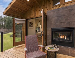 Une terrasse en bois avec un foyer, une chaise et une table sur laquelle se trouvent un livre et des tasses.