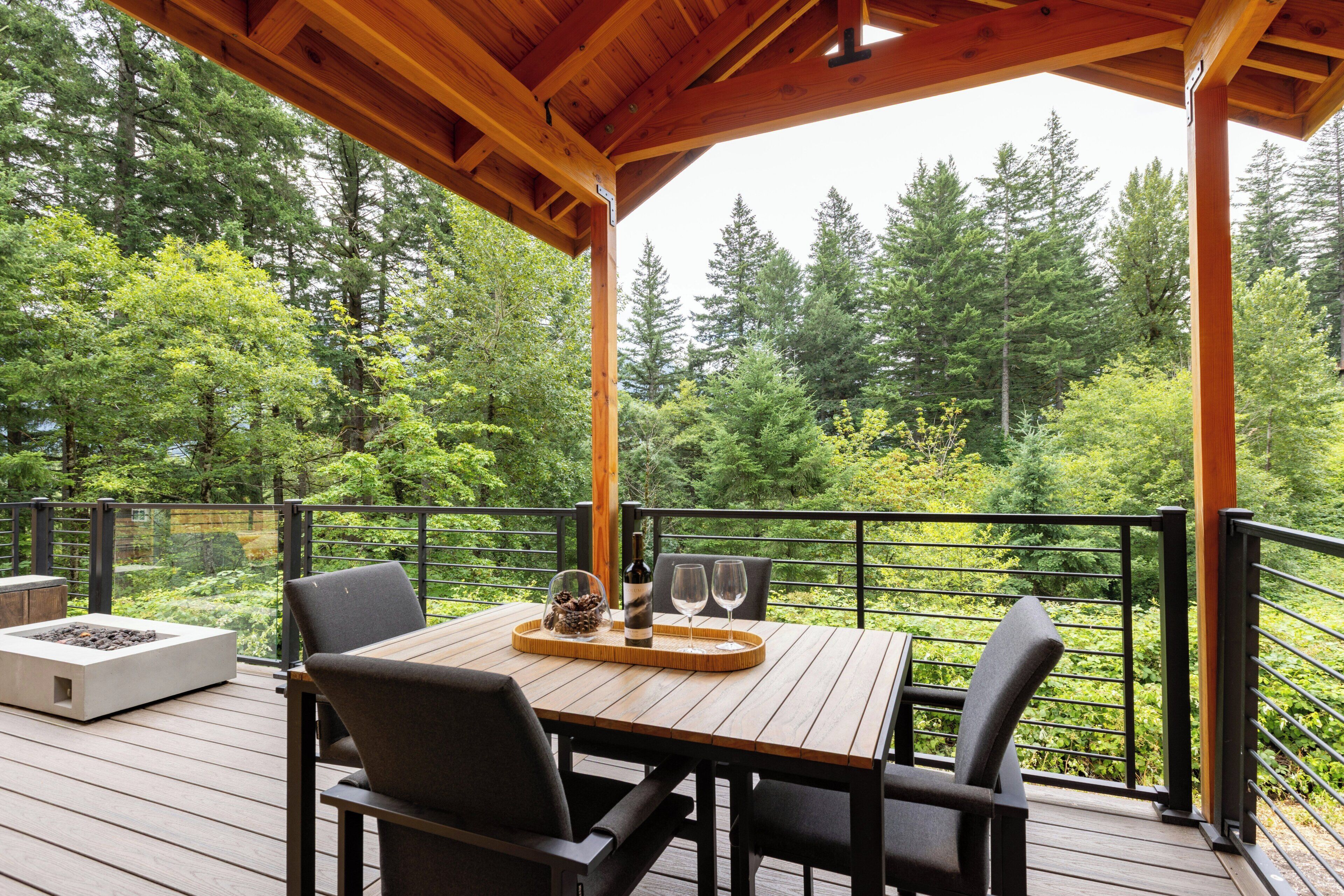 Una terraza de madera con una mesa y sillas, con vista a un área boscosa.