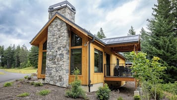 A modern house with a stone chimney, large windows, and a wooden deck.