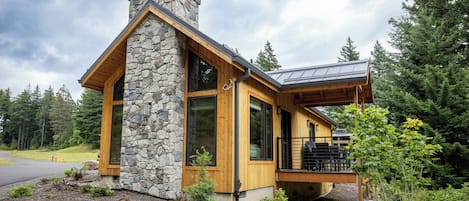 Une maison moderne avec une cheminée en pierre, de grandes fenêtres et une terrasse en bois.