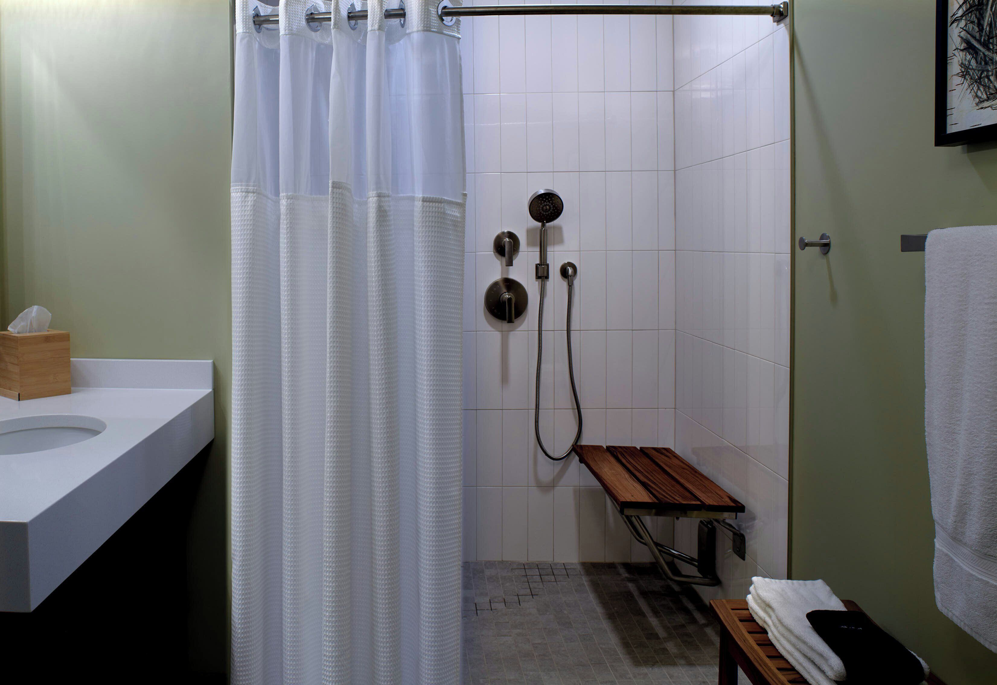 Un baño con ducha, un banco de madera, un perchero y un lavamanos.