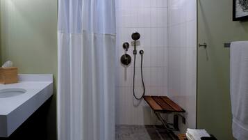Un baño con ducha, un banco de madera, un perchero y un lavamanos.