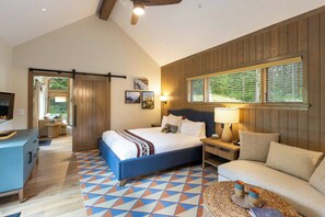 A bedroom with a bed, bedside tables, a sofa, a wooden wall, and a window with blinds.