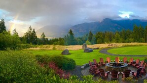 A circular outdoor seating area with chairs around a central fire pit, set in a landscaped garden with a mountain backdrop. - Skamania Lodge (Stevenson)