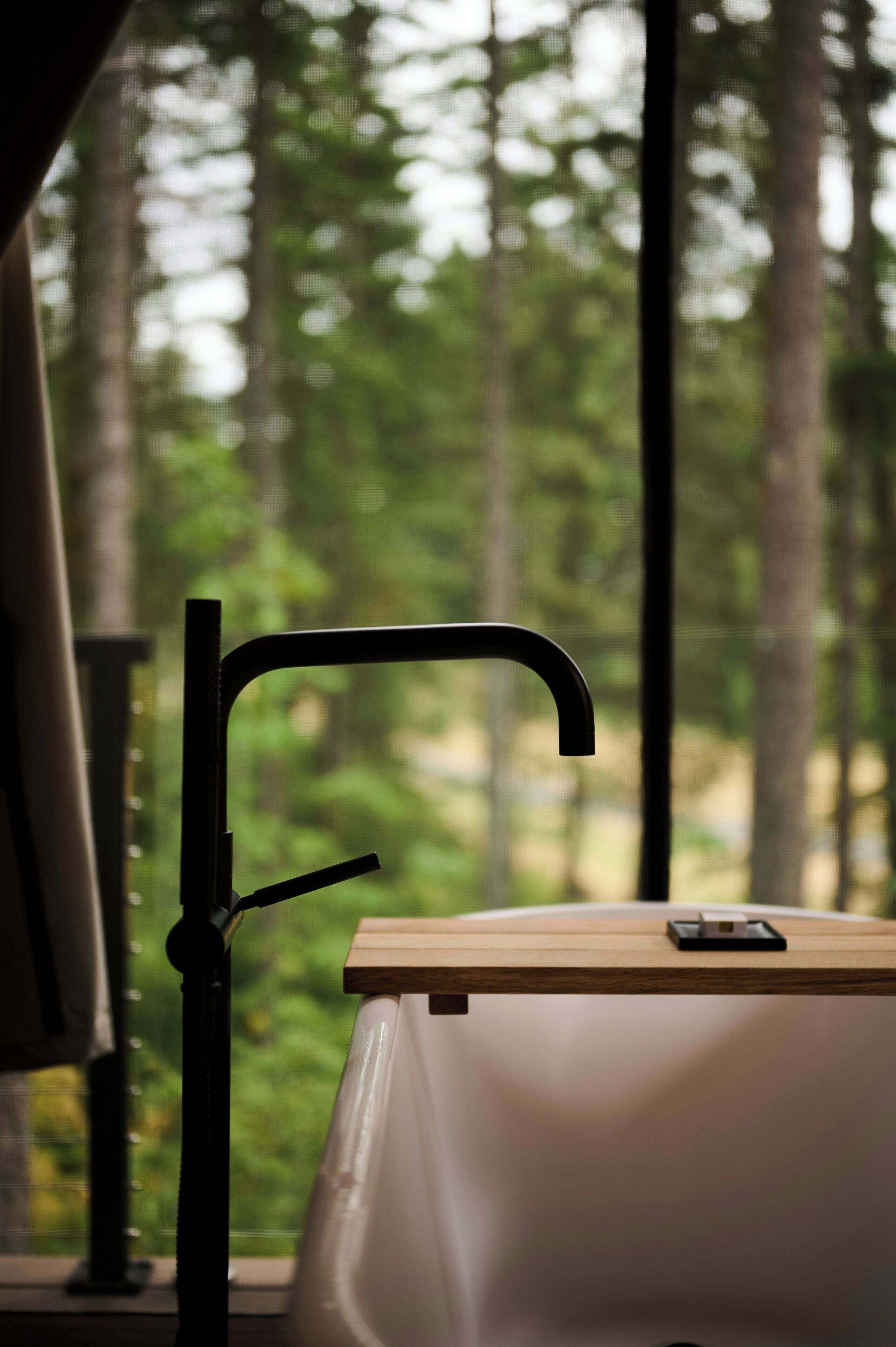 A bathroom with a modern faucet, a wooden counter, and a view of a forest through a window.