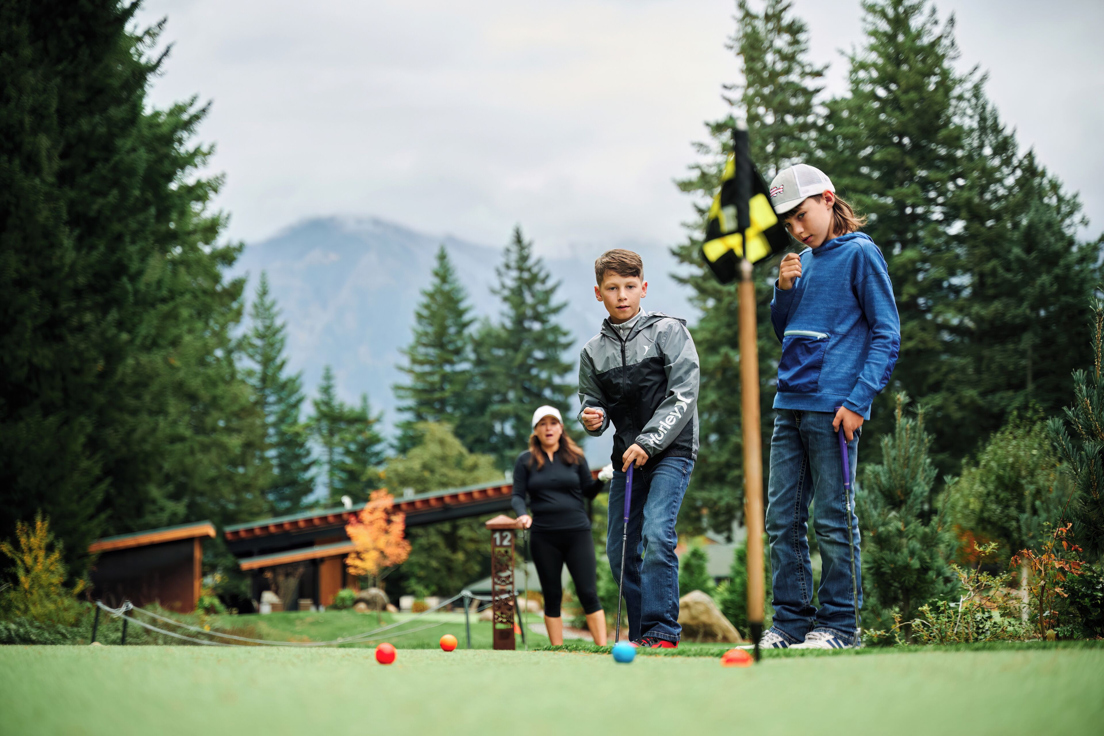 A golf course with a wooden structure, a flag, and a mountain in the background.