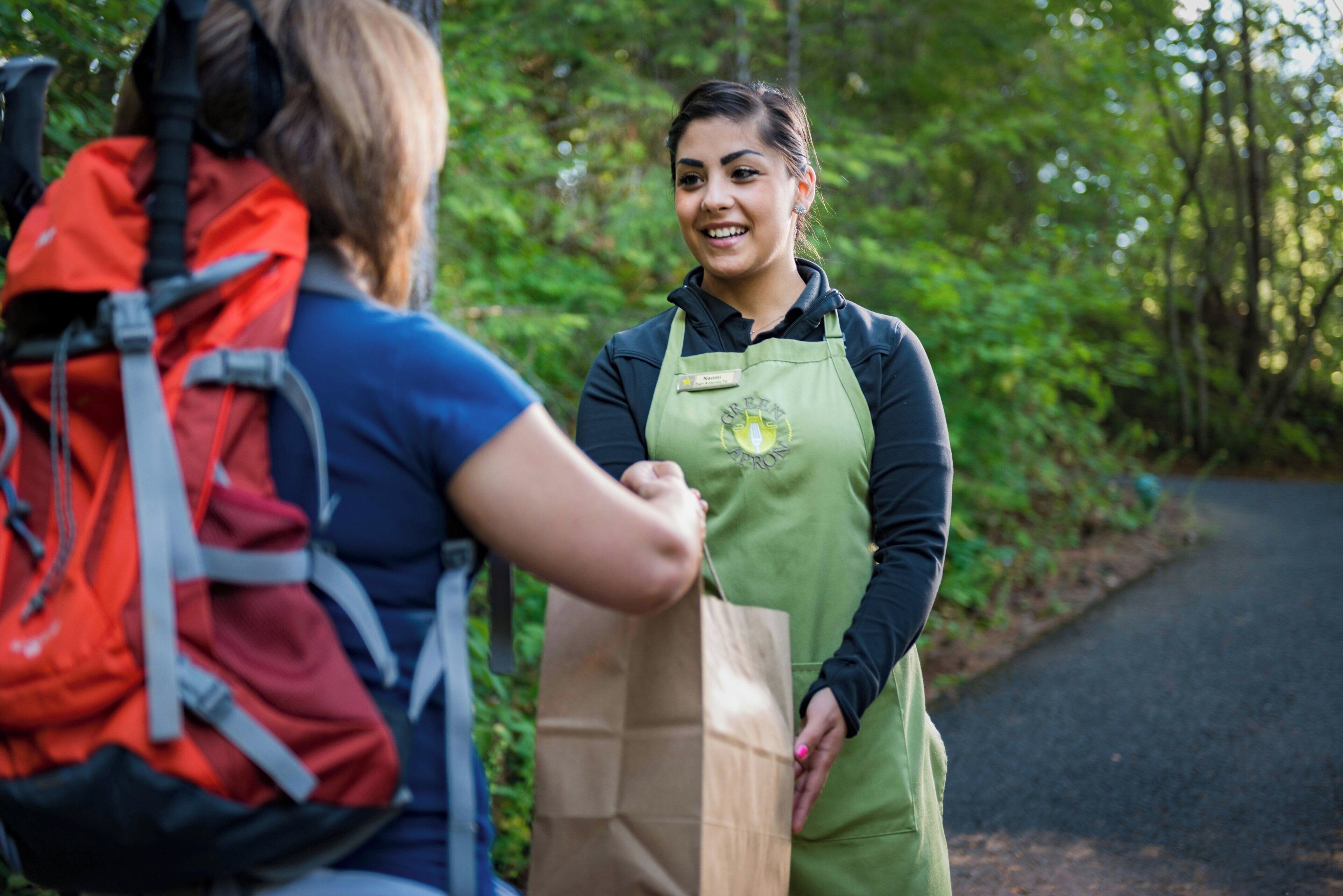A person in a green apron standing on a path with greenery on both sides.