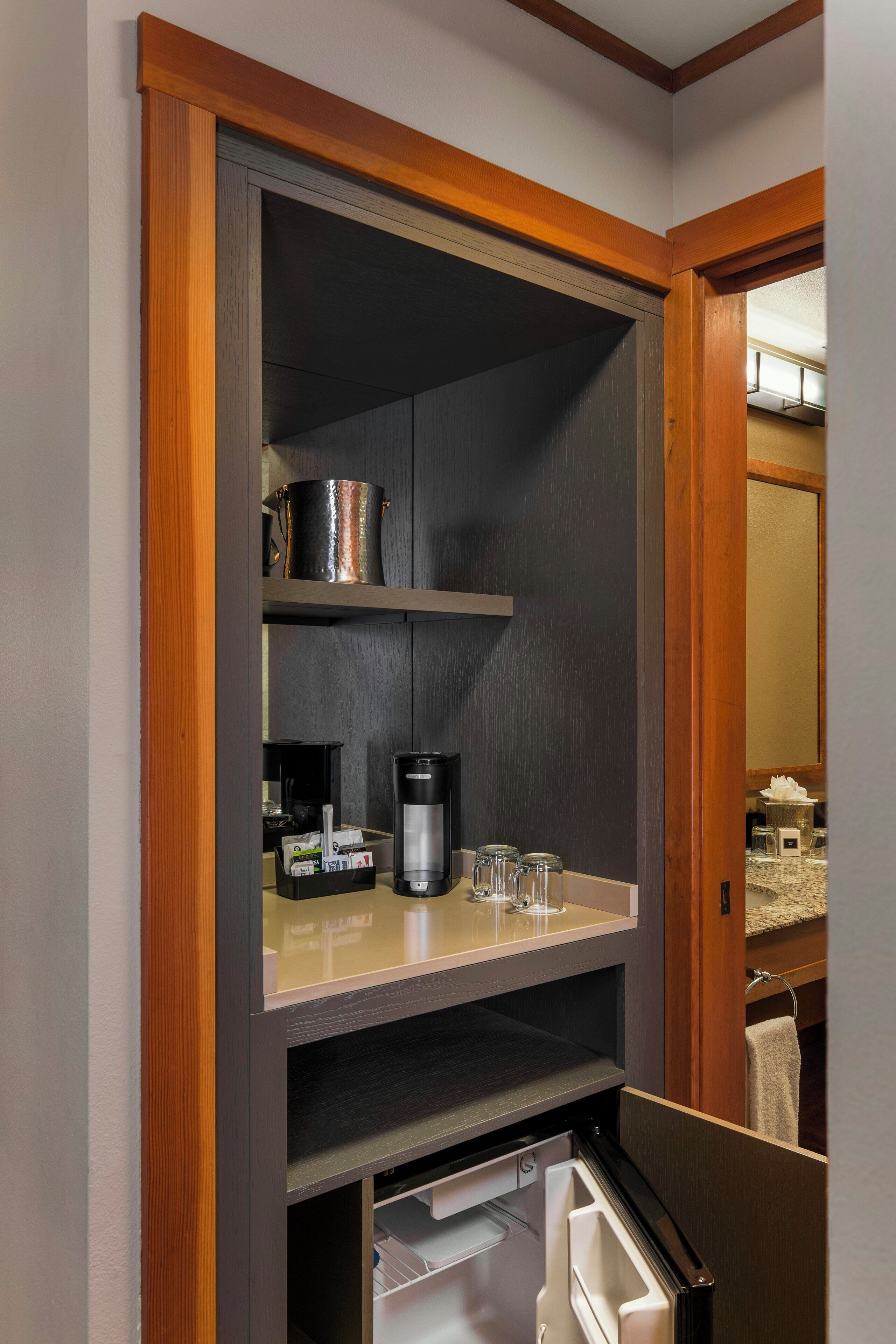 A compact kitchenette with a coffee maker, a kettle, and a glass jar on the countertop.