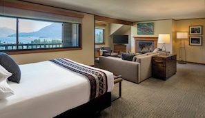 A hotel room with a bed, a sofa, a fireplace, a television, and a view of mountains.