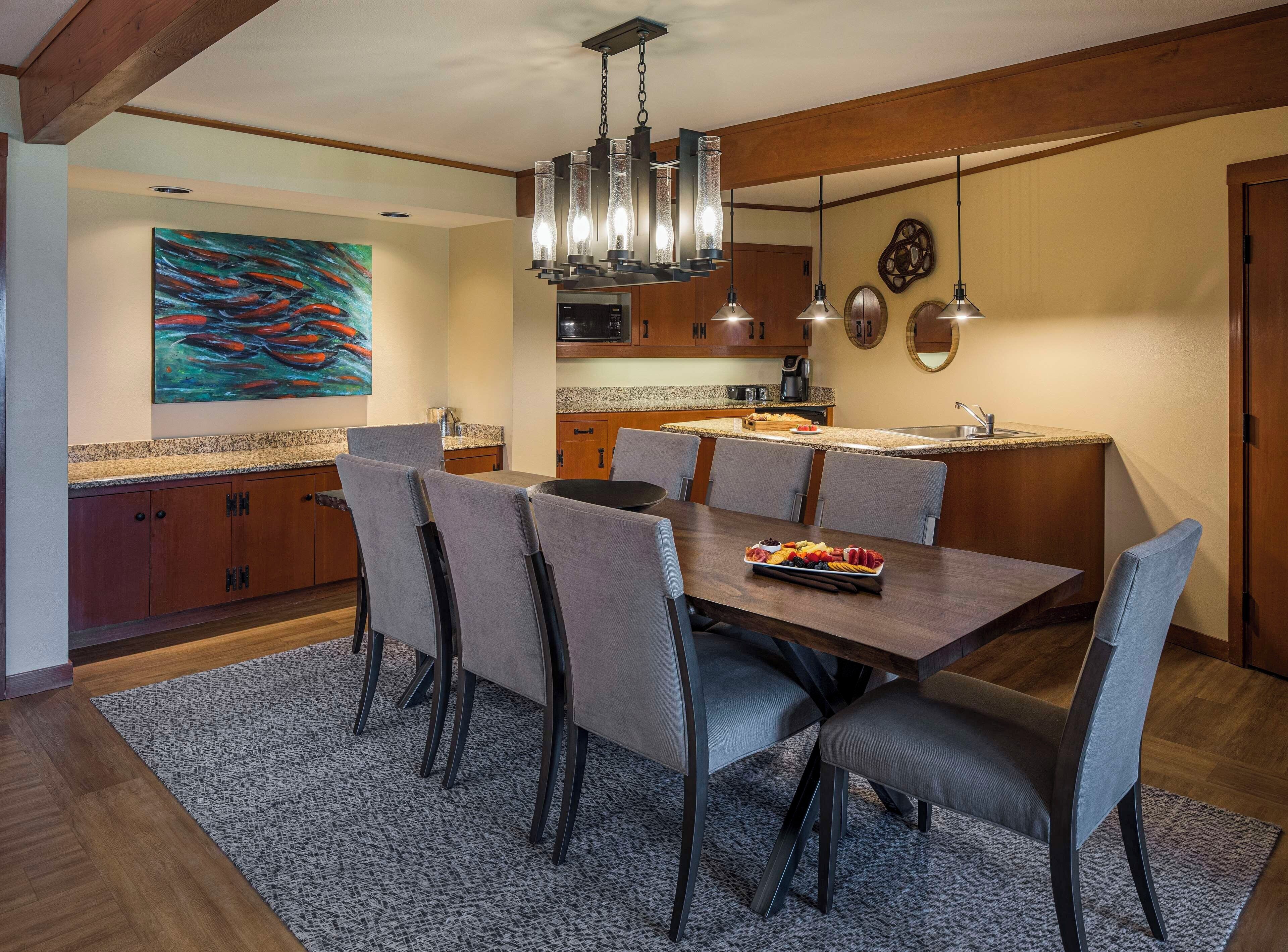 Un comedor moderno con una mesa de madera, sillas tapizadas en gris y una araña.
