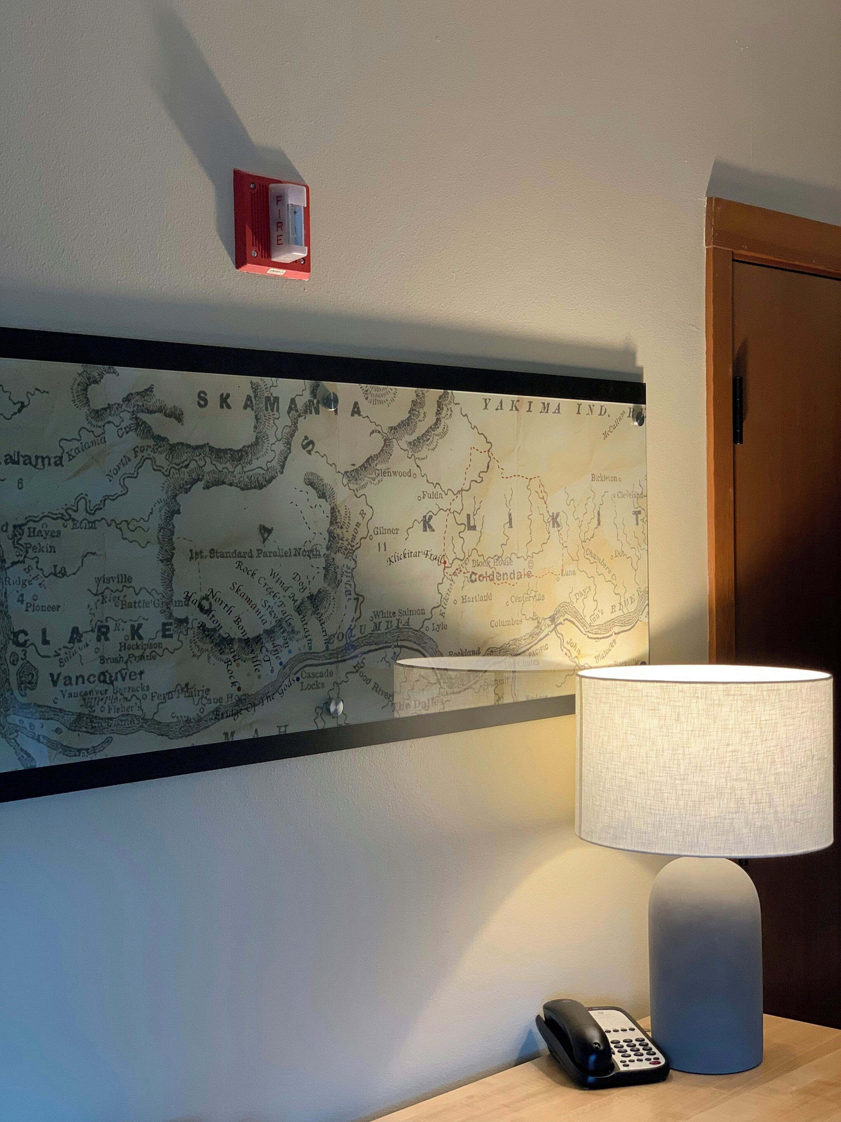 A map on a wall with a lamp and a phone on a table.