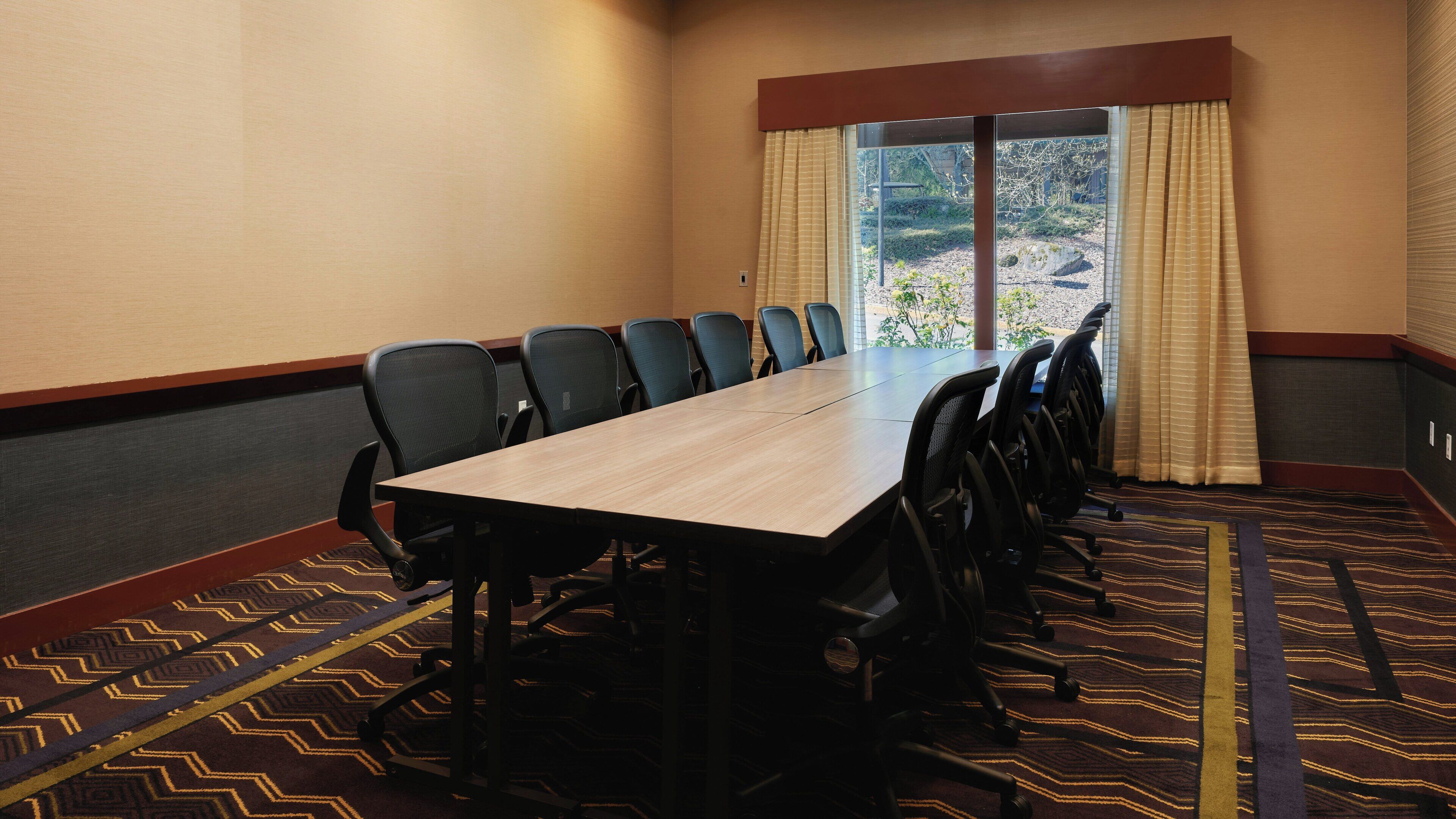 A conference room with a long table and multiple chairs, a patterned carpet, and a window with curtains.